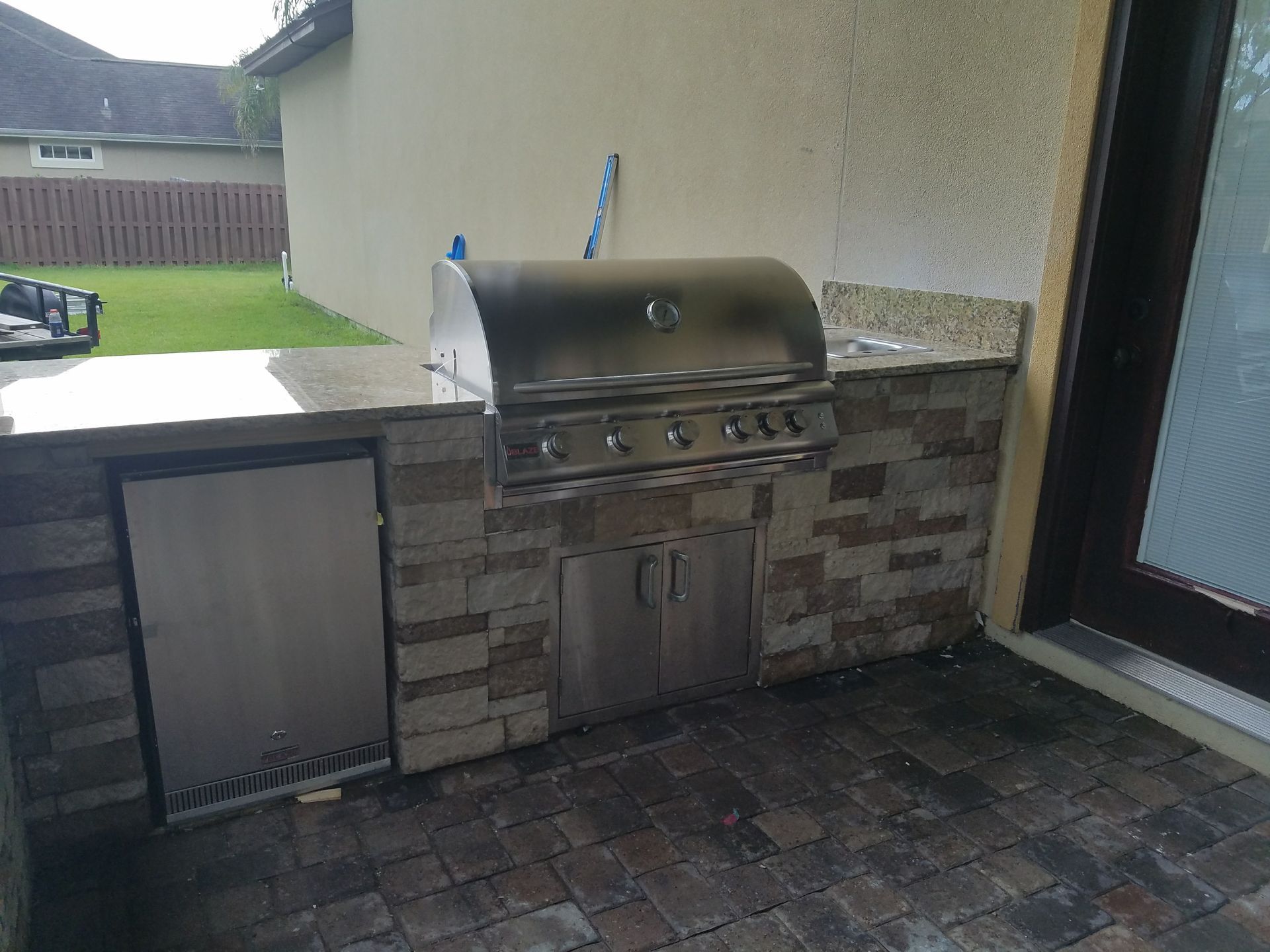An outdoor kitchen with a grill and a refrigerator.