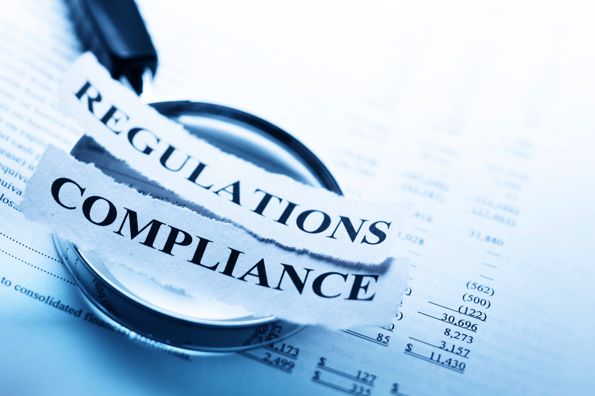A magnifying glass is sitting on top of a piece of paper that says regulations compliance