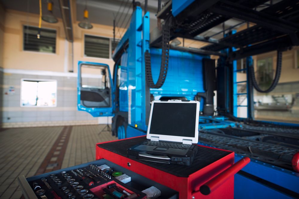 Laptop on red cart in industrial garage with blue truck lift and workshop windows