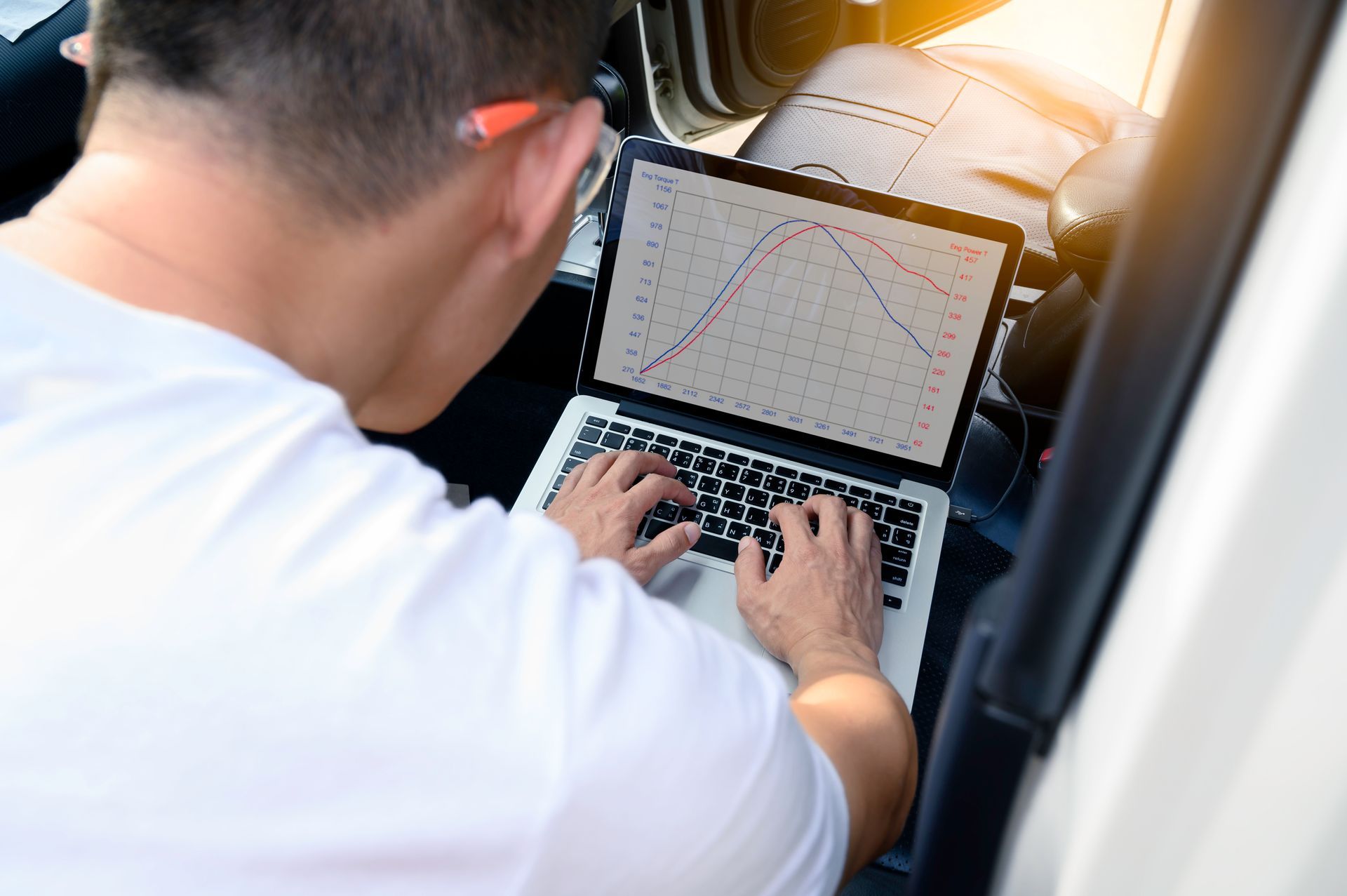 Person typing on a laptop displaying charts in a car
