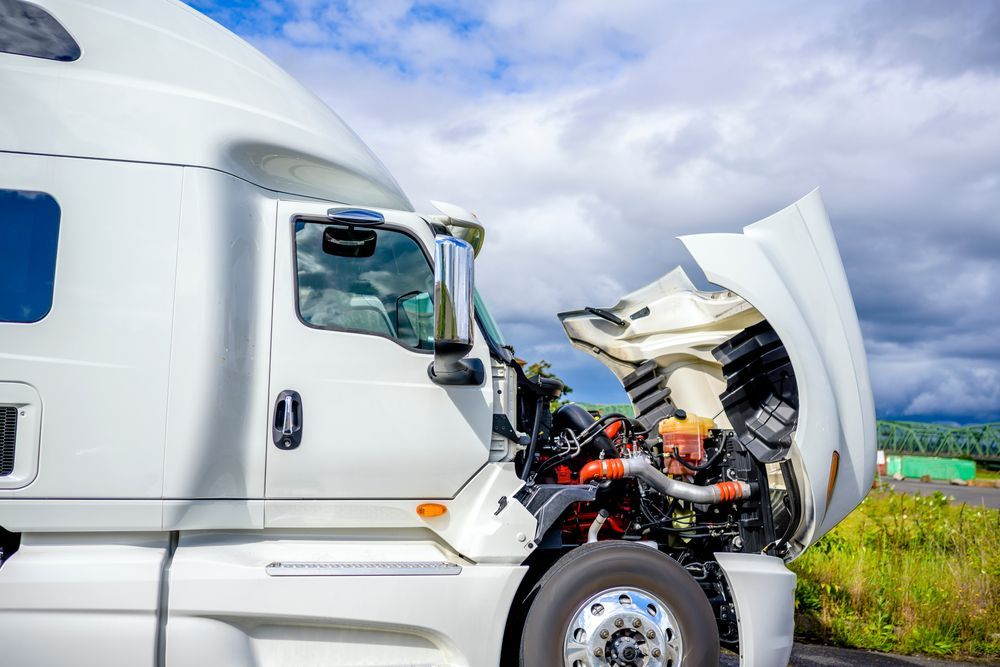 White semi-truck with front-end damage after a collision on a roadside under a cloudy sky