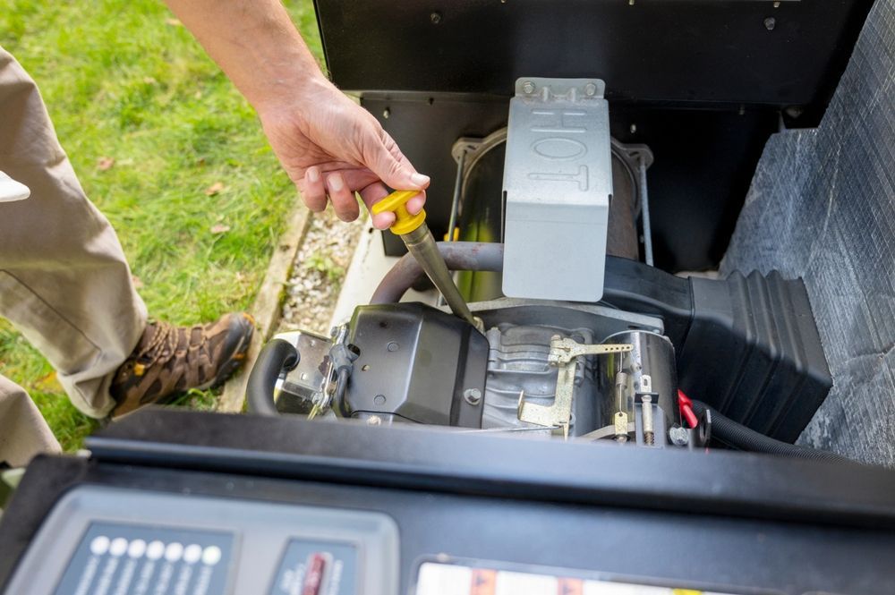 Hand reaching into an open machinery compartment beside a gray engine unit outdoors.