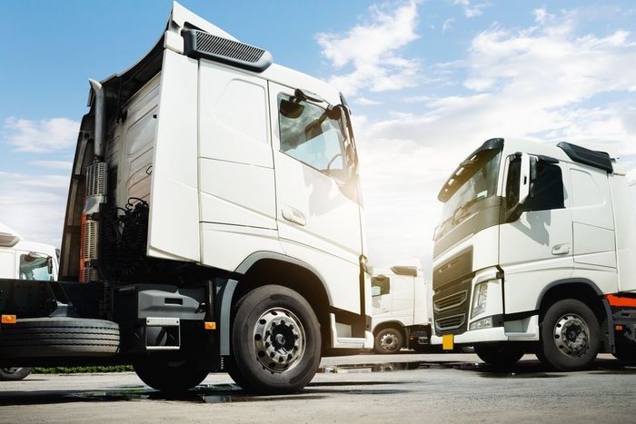 Two white semi trucks parked facing each other on a sunny lot