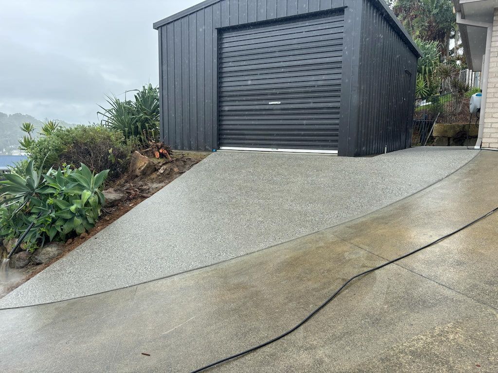 A black garage with a concrete driveway leading to it.