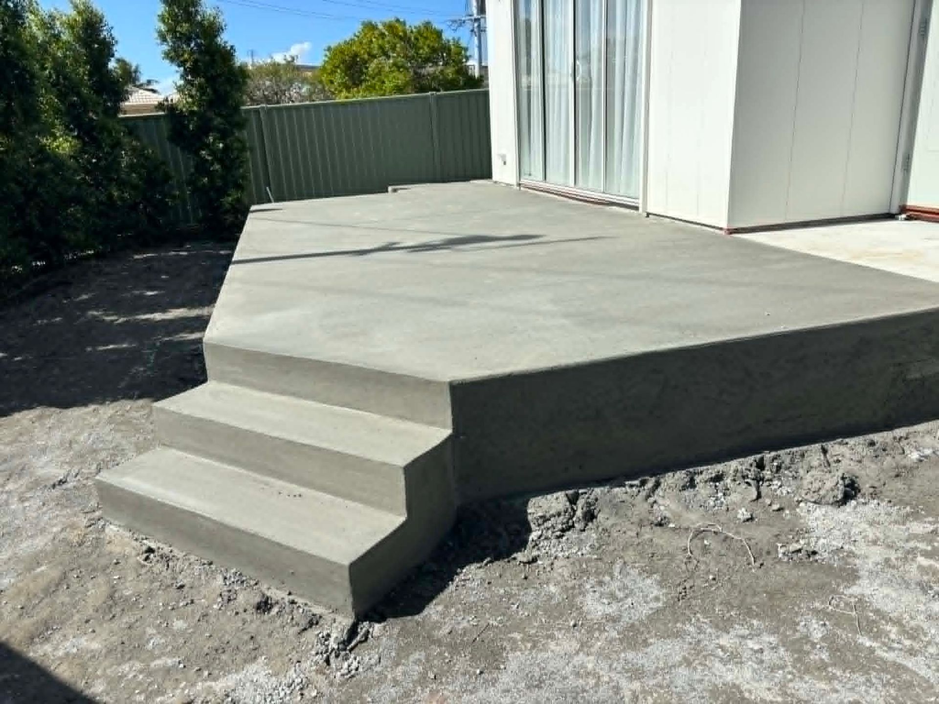 Concrete patio with small steps beside a white shed in a backyard