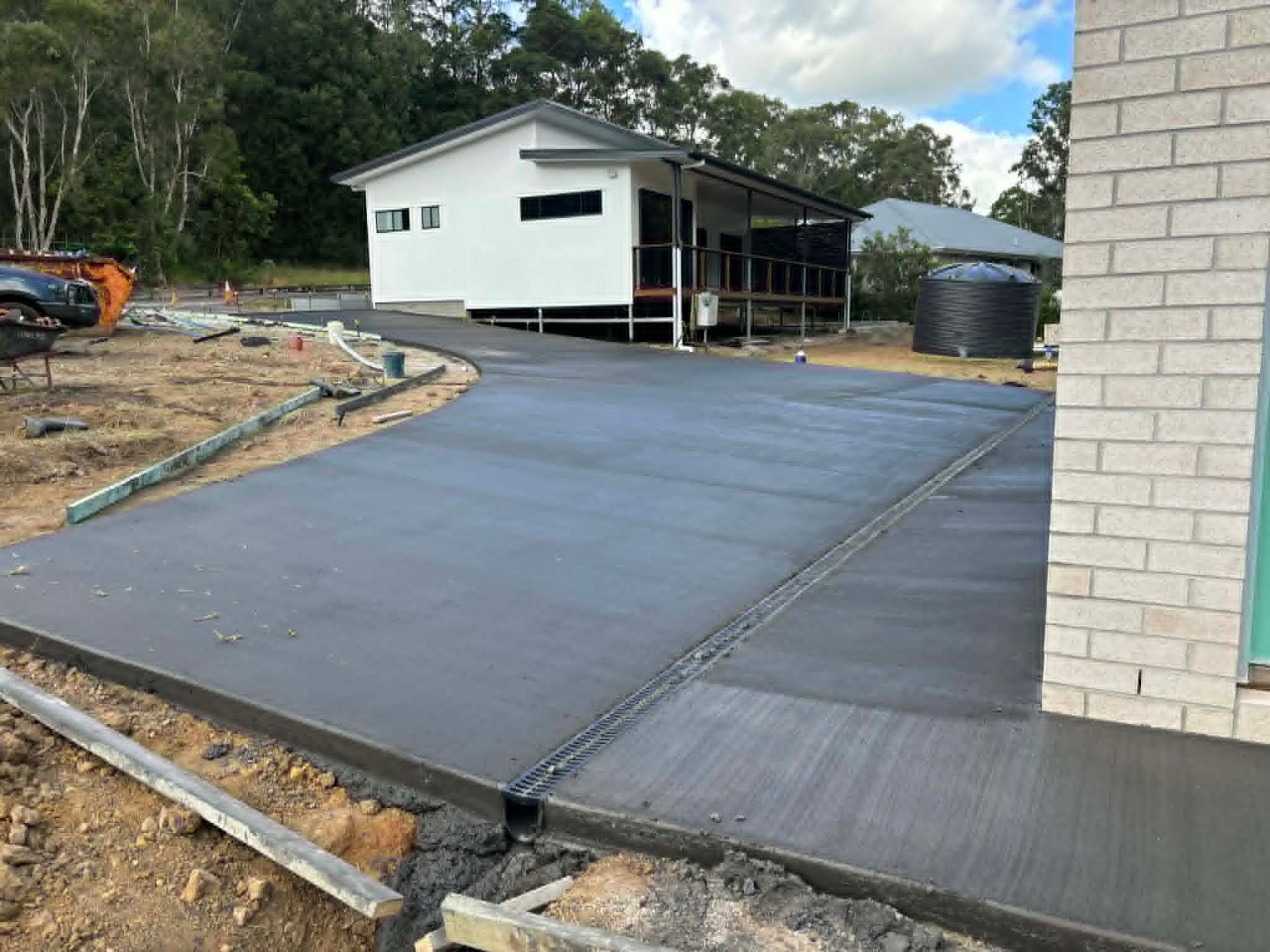 Concrete driveway and ramp leading to a white house under construction beside a brick wall