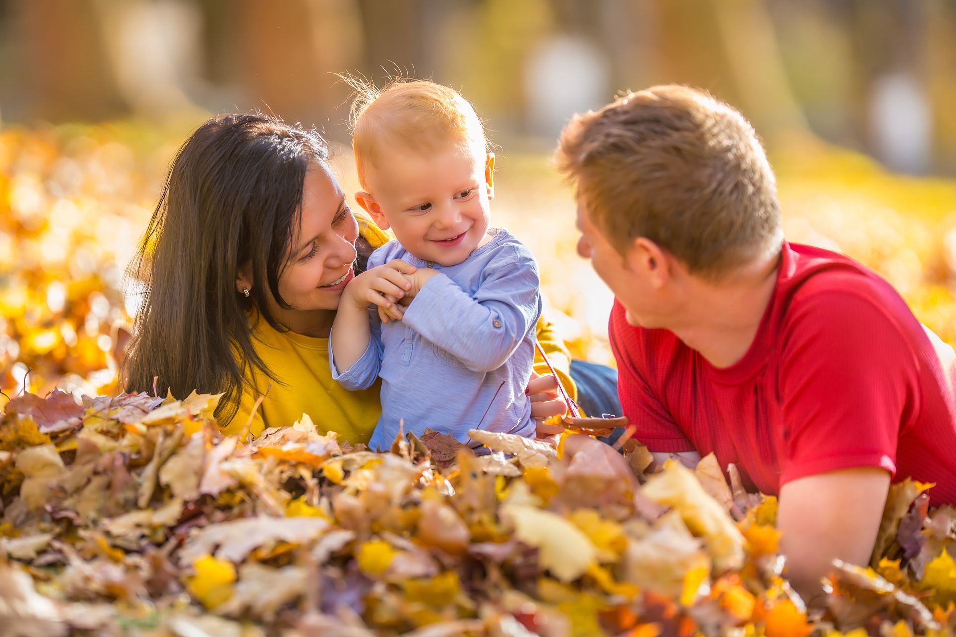 A family is laying in a pile of leaves with a baby.