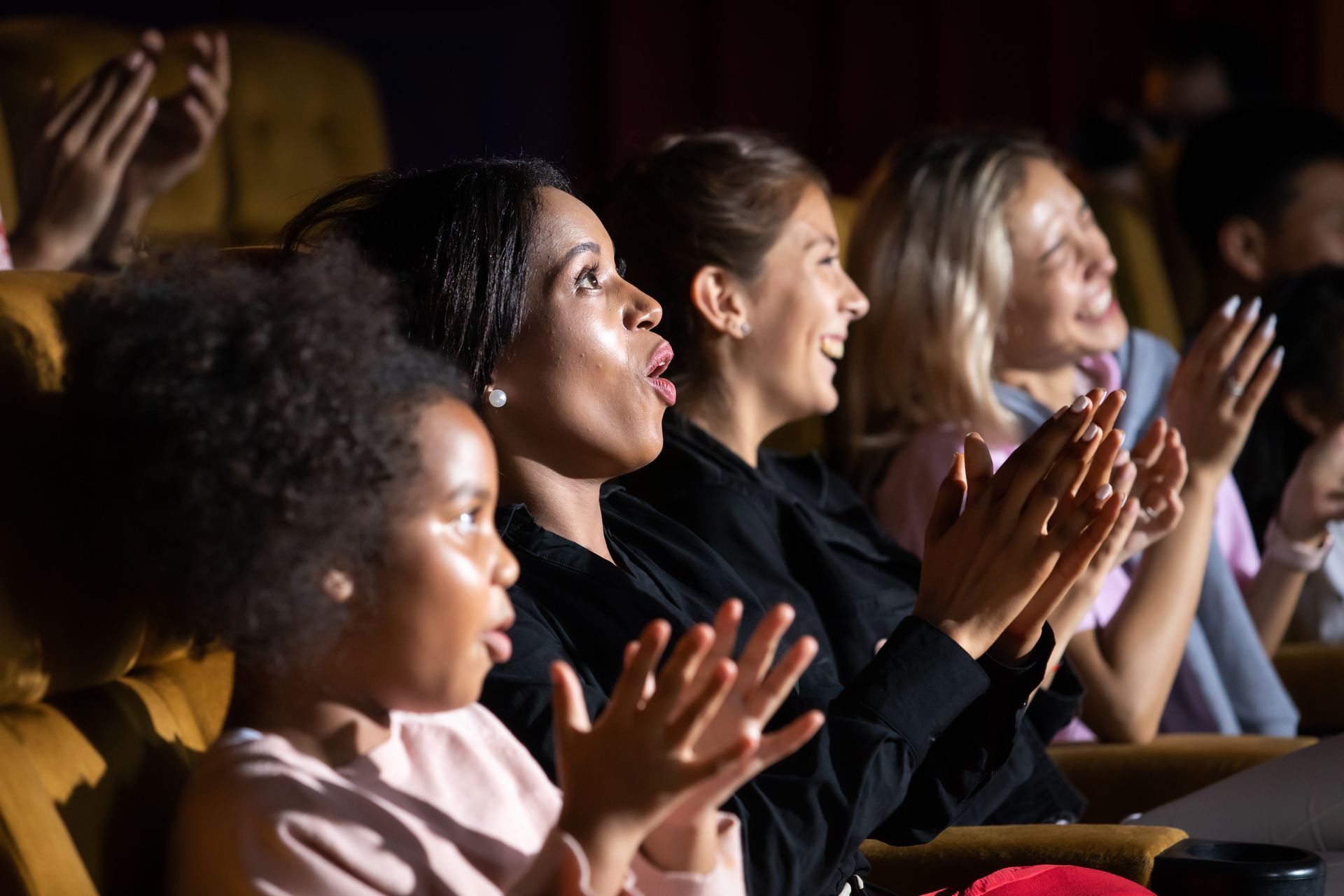 A group of people are sitting in a theater clapping their hands.