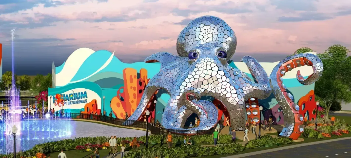 An aquarium with a large octopus sculpture in front. There's a fountain in the foreground and colorful building.