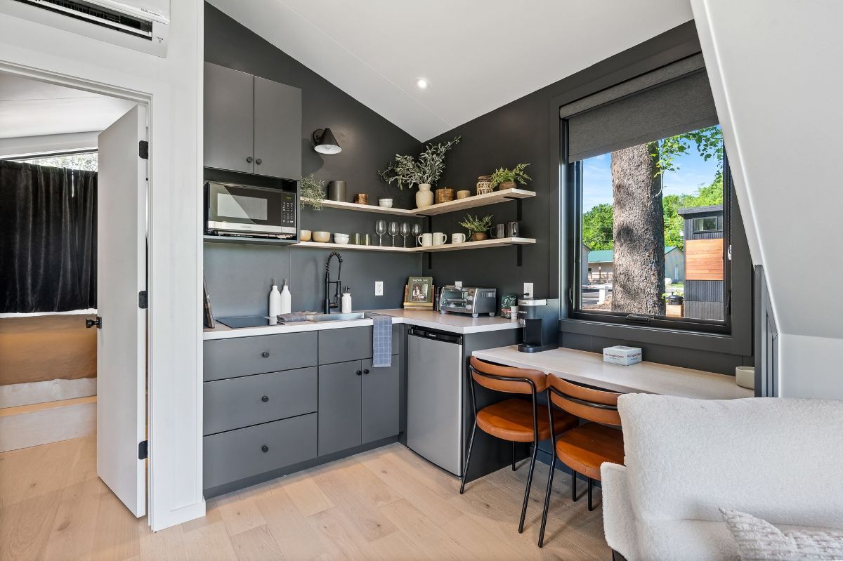 Small gray kitchen with a window, shelves with plants, and a small table with two chairs.