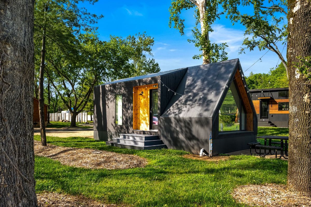 A-frame cabin with a black exterior and yellow door in a wooded area.