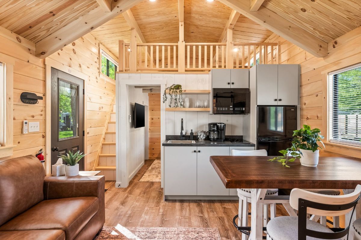Interior of a tiny house with a kitchen, living area, and loft. Light wood and modern décor.