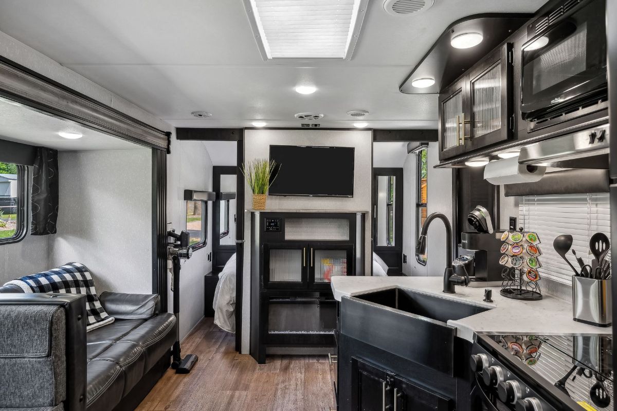 Interior of a modern RV with kitchen, living, and bedroom areas; gray, black, and wood tones.