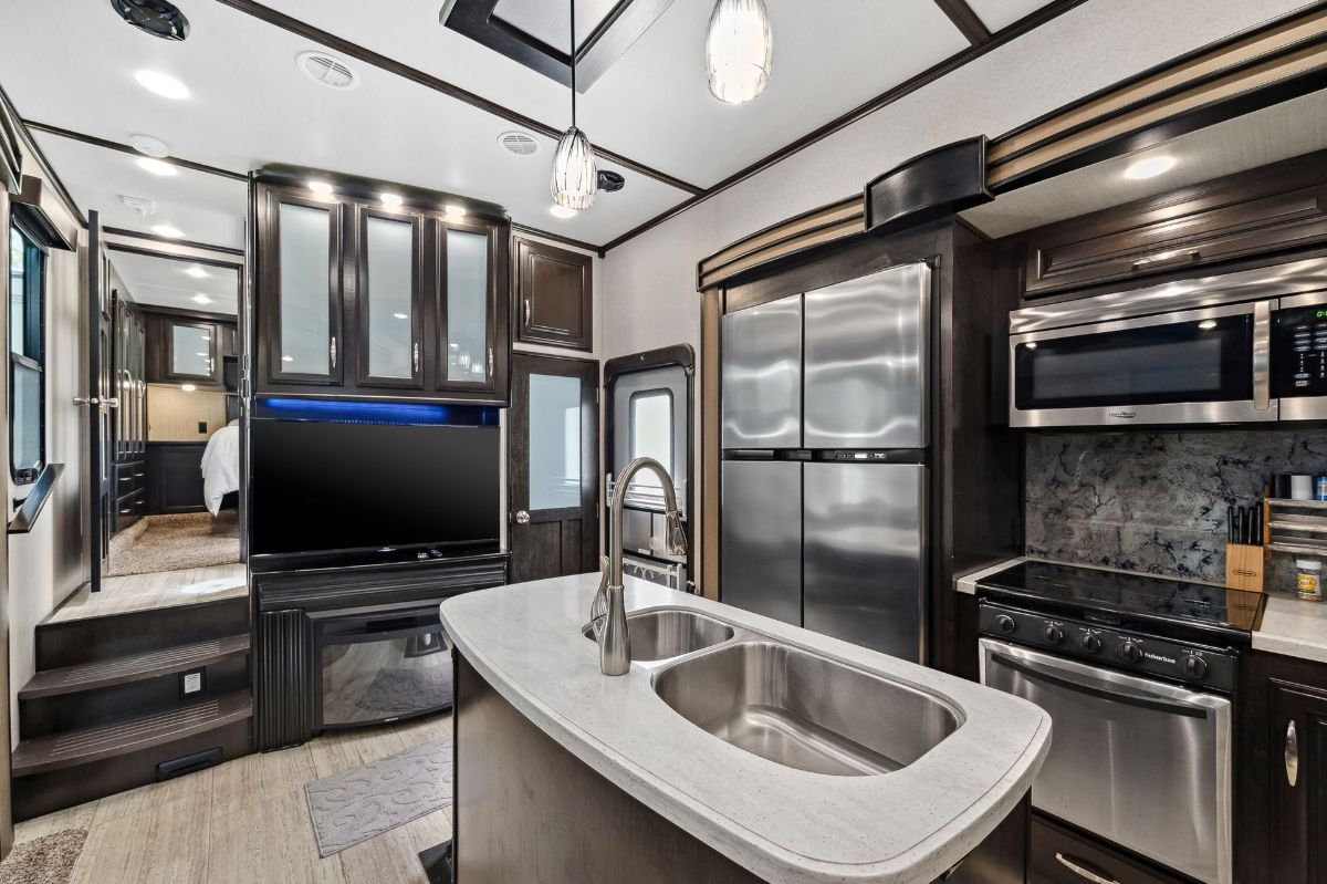 Interior of a luxurious RV kitchen with stainless steel appliances, dark cabinets, and an island with a sink.