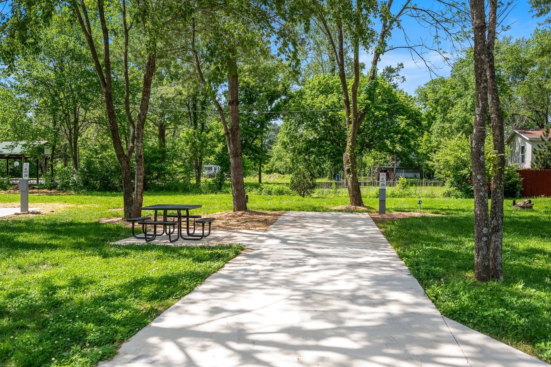 Concrete path through a park with trees, picnic table, and green grass.