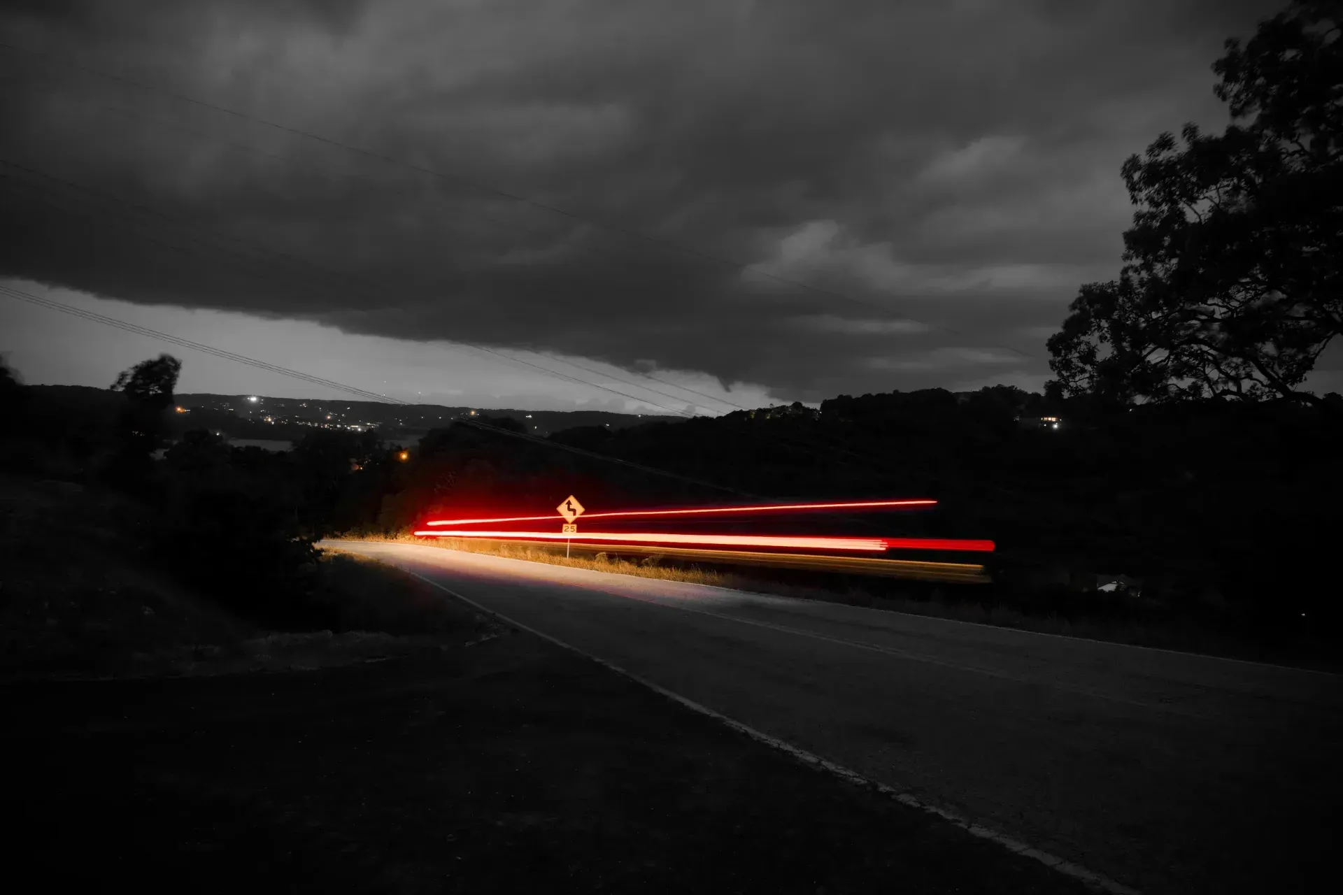 A black and white photo of a car driving down a road at night.