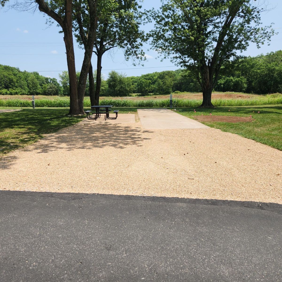 Empty campsite with gravel surface, picnic table, trees, and grassy background.