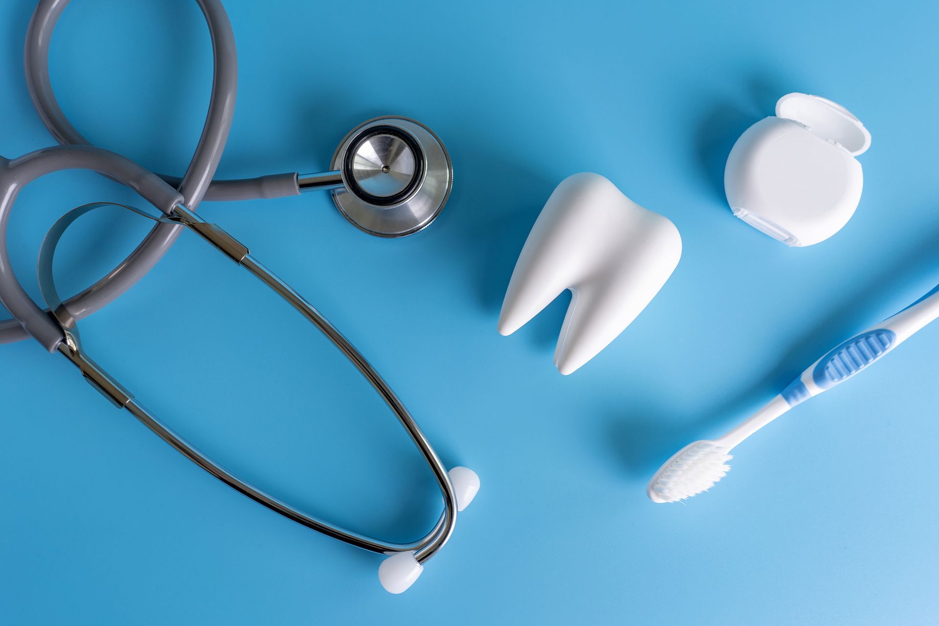 A tooth , toothbrush , stethoscope and floss are on a blue surface.