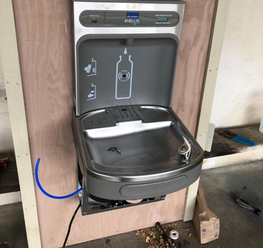 Drinking fountain with bottle filler at Saint Mary's High School, silver and gray with a blue water tube.