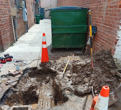 A drain pipe being cleared with a snake tool, next to a red watering can.