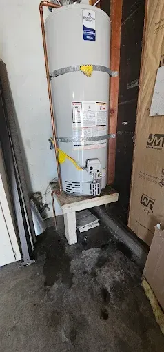 Water heater in a garage, leaking water onto the floor.