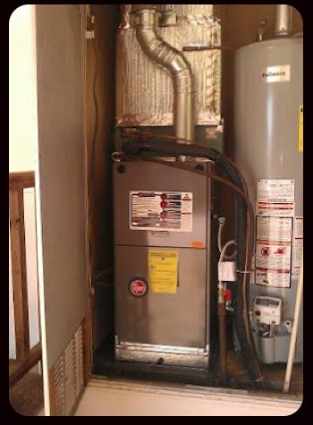 Indoor HVAC furnace and water heater in a utility closet with exposed ductwork and pipes.