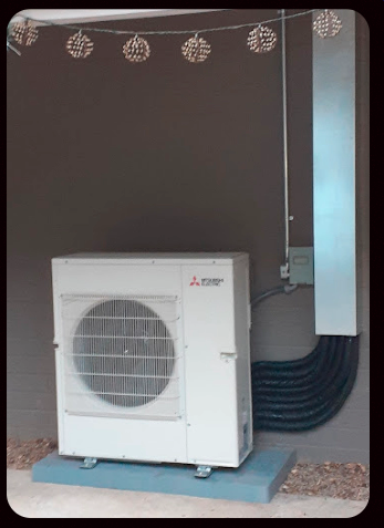 Outdoor Mitsubishi mini-split AC unit beside a wall-mounted electrical box and conduit.