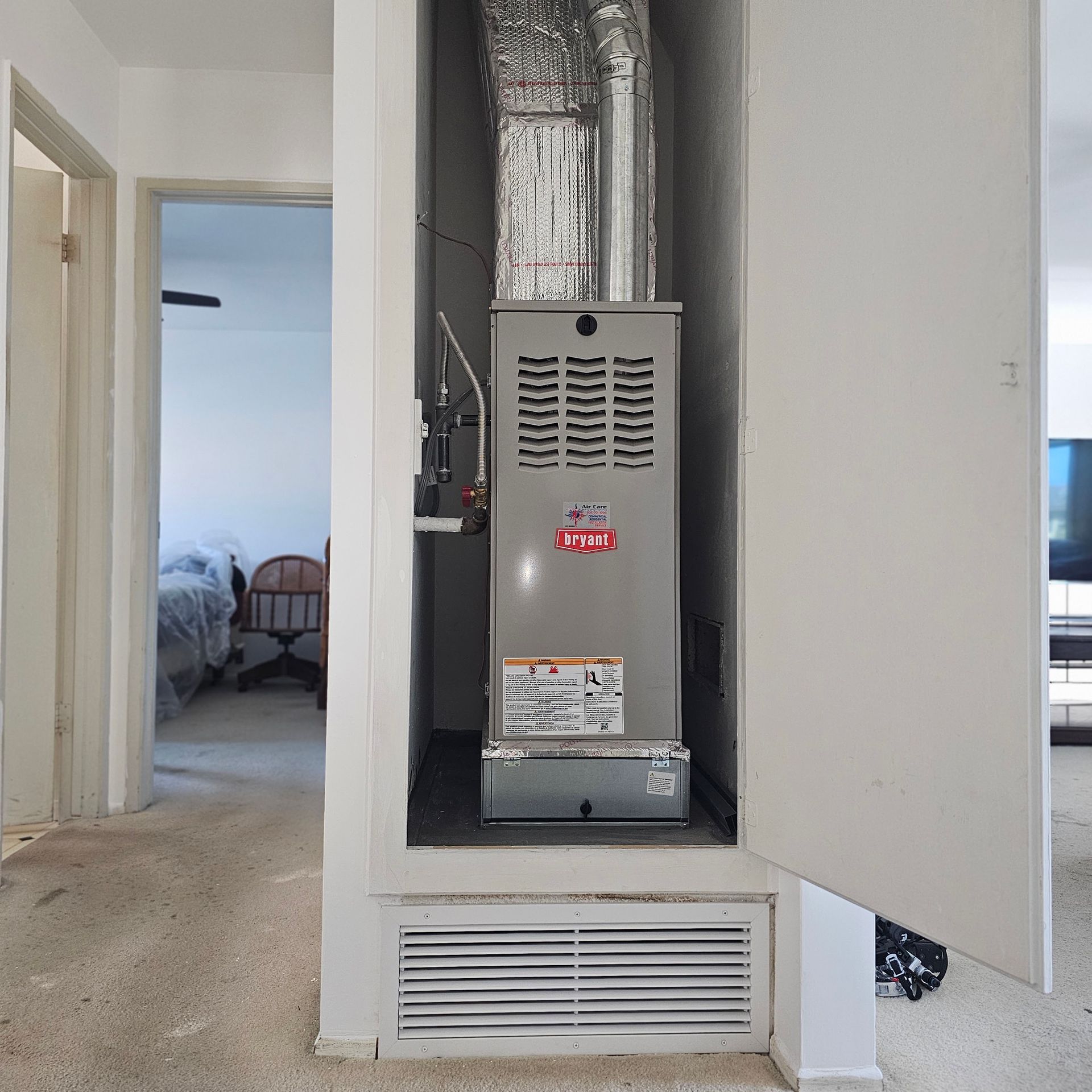 Open wall closet with a silver HVAC furnace unit and vent grille in a hallway
