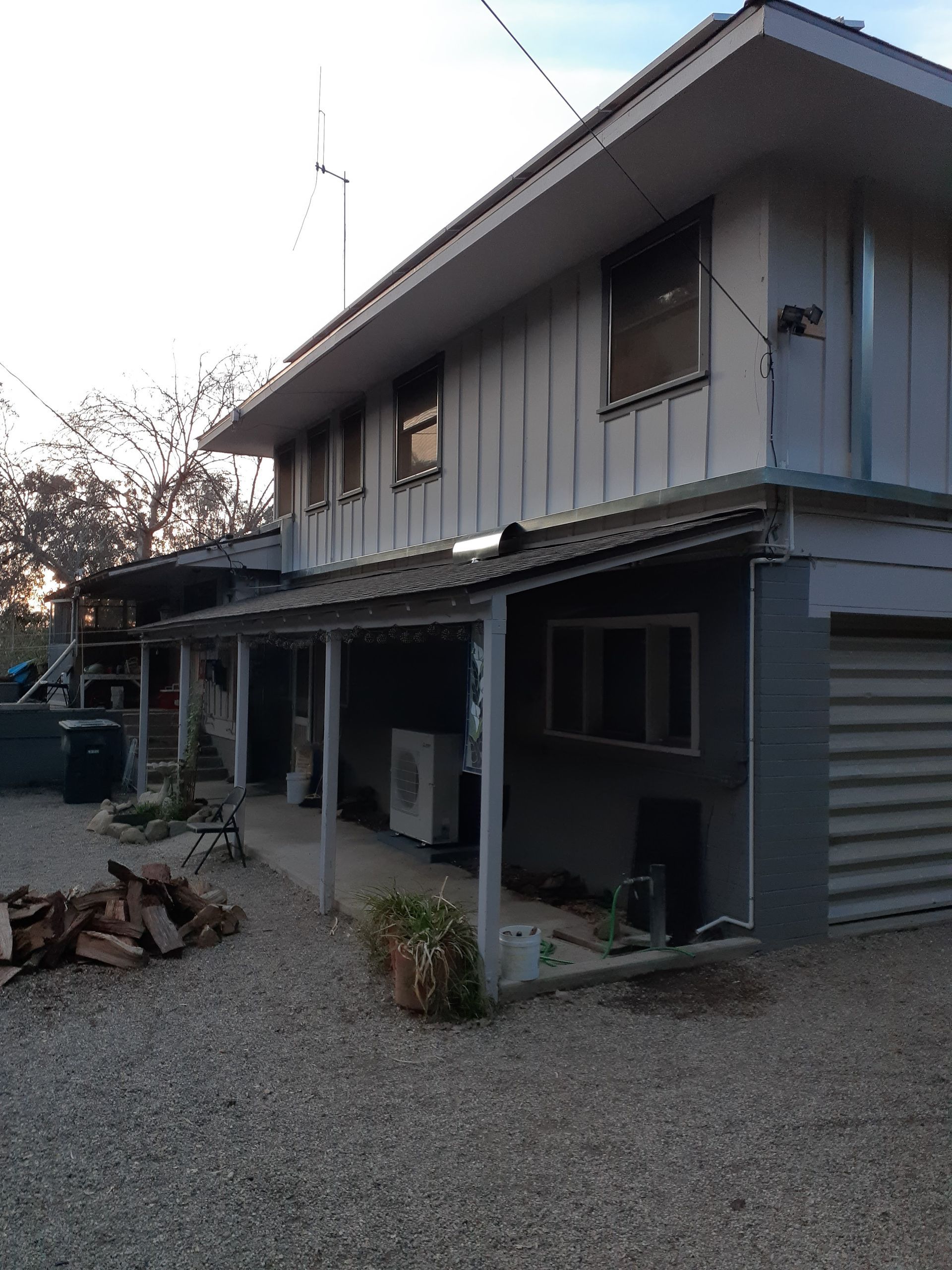 Two-story gray house with a covered porch and gravel yard at dusk