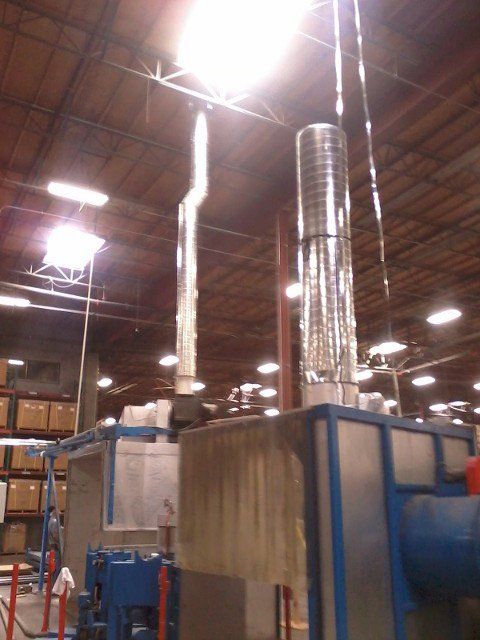 Industrial warehouse with large blue machinery and silver ventilation ducts under bright ceiling lights