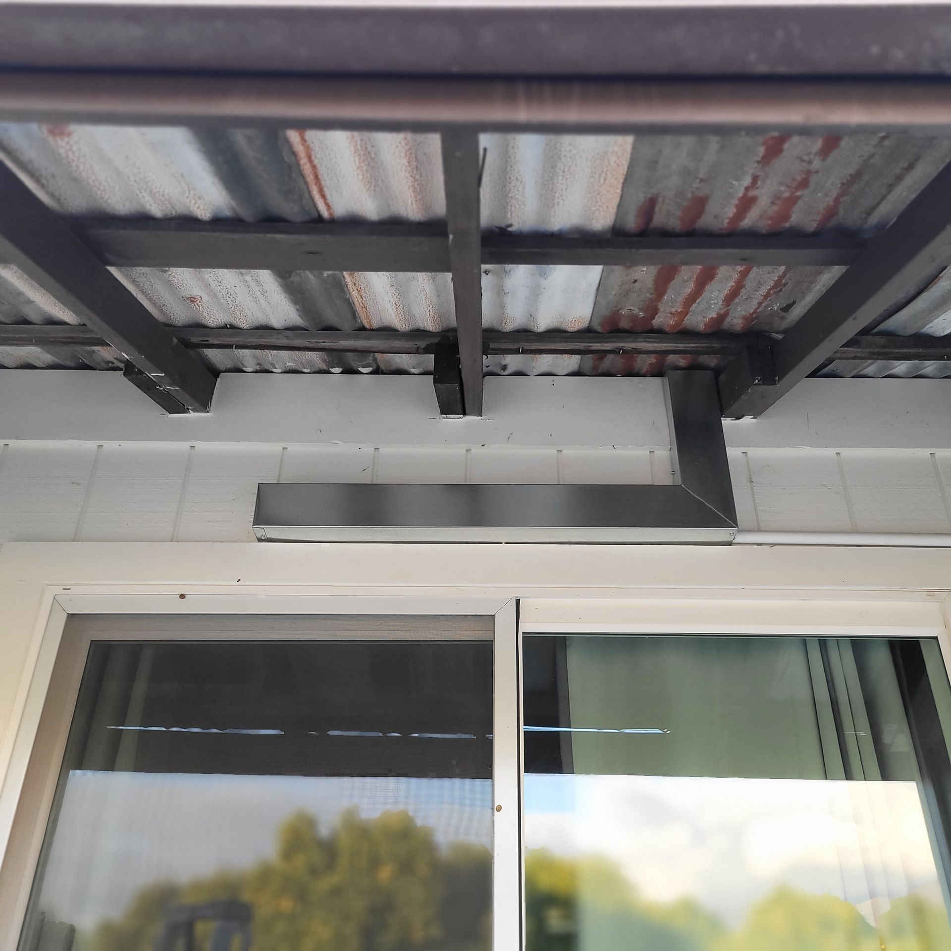 Exterior of a building entrance with a sliding glass door and corrugated metal awning overhead