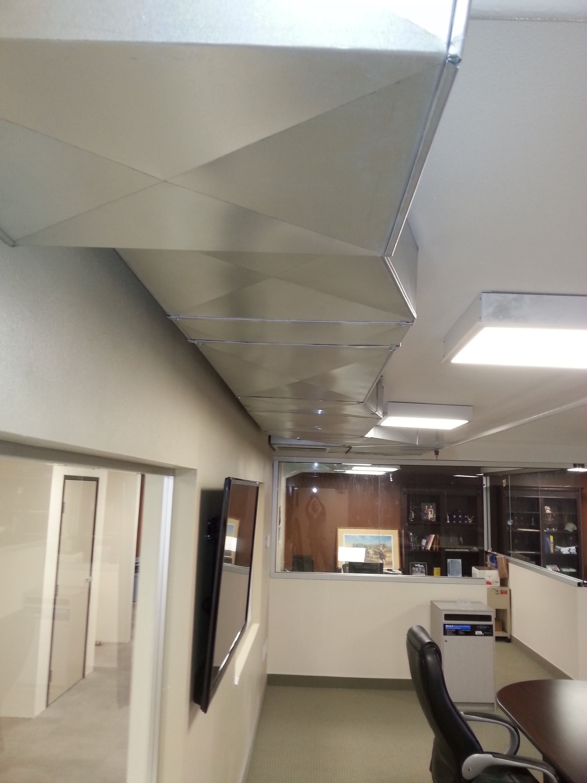 Office meeting room with ceiling ductwork, fluorescent lights, conference table, chairs, and cabinets
