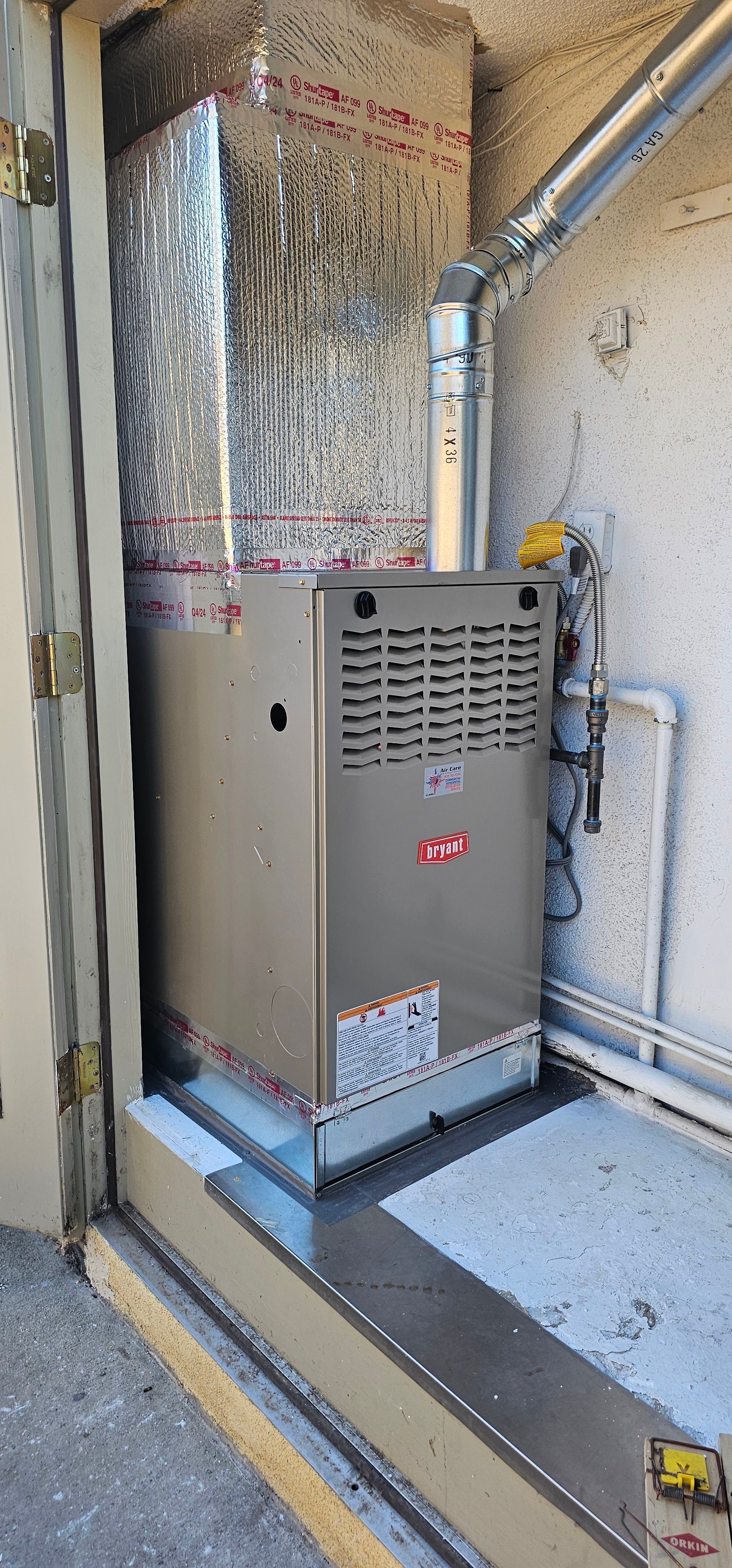 Indoor furnace unit in a utility closet, with exposed ducting and pipes.