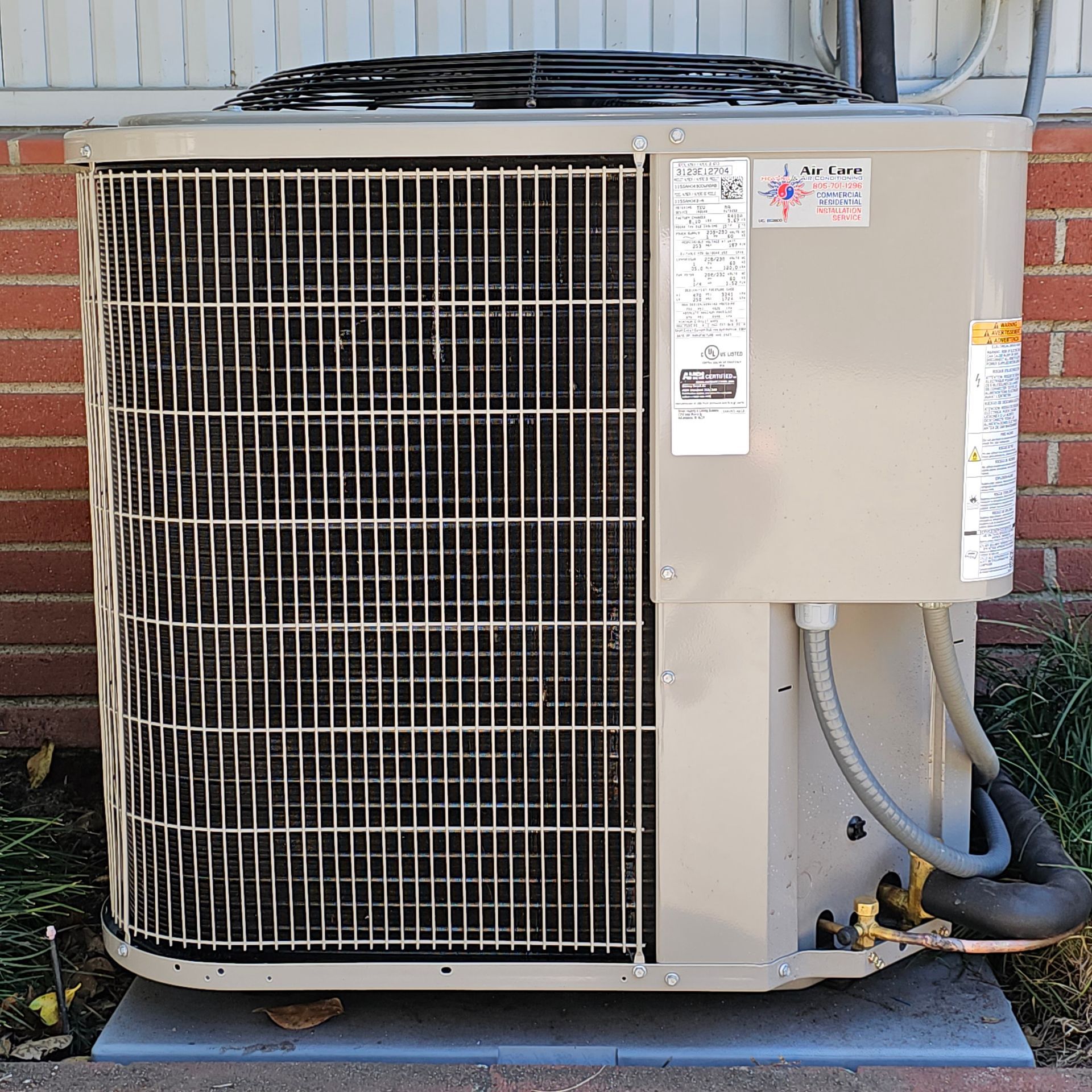 Outdoor air conditioning unit with a large fan grille and beige casing on a concrete pad.