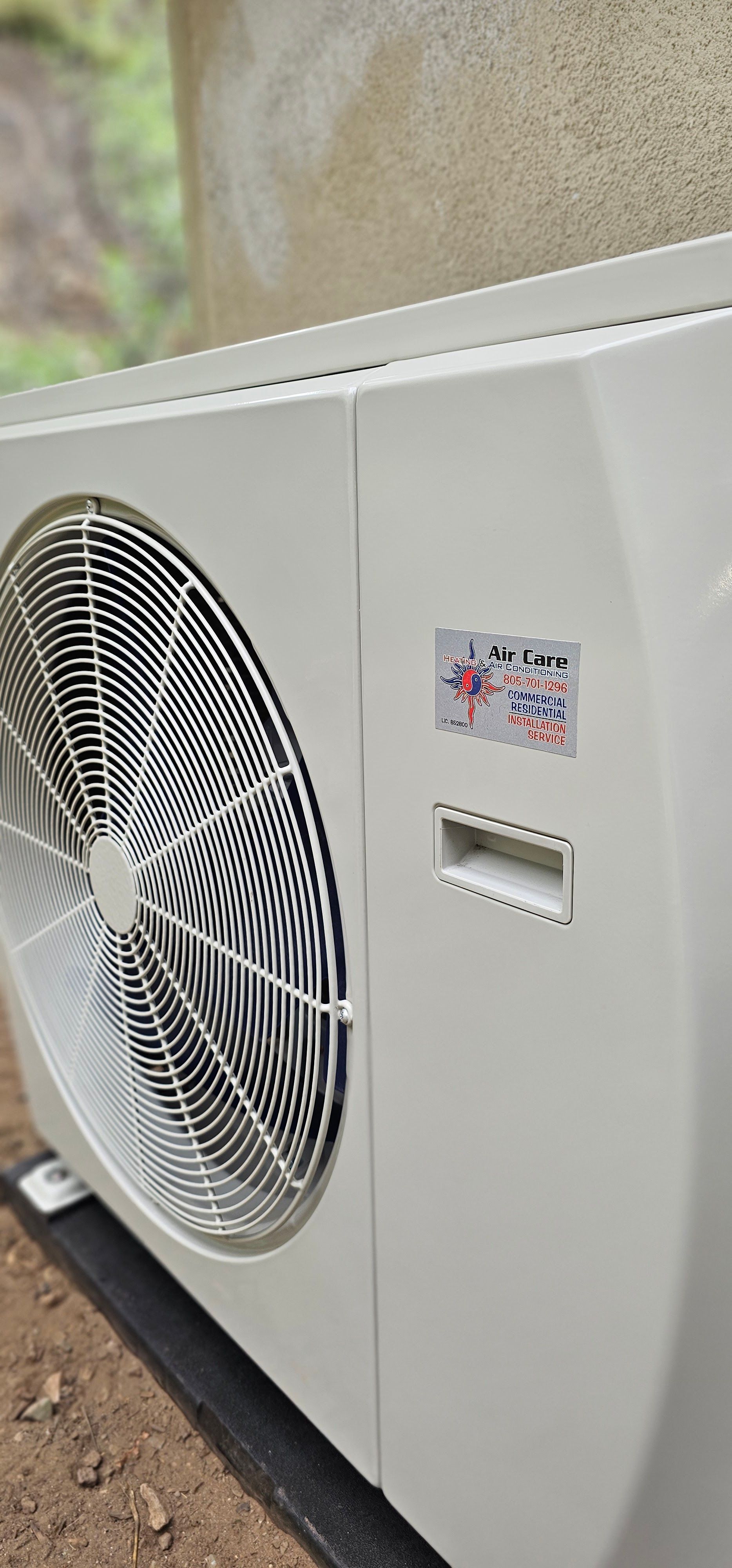 White outdoor air conditioner unit with a large fan against a wall