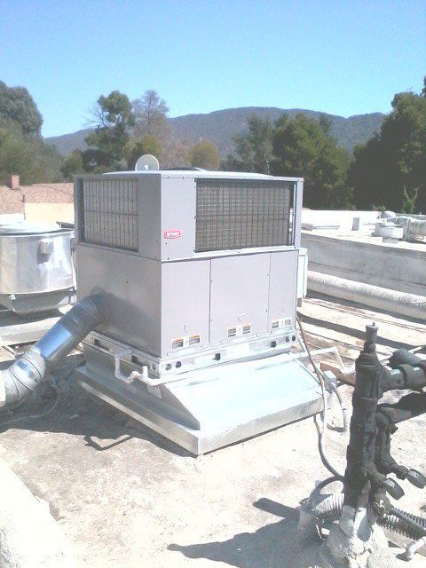 Rooftop HVAC unit with ducts, set against a bright sky and distant hills.