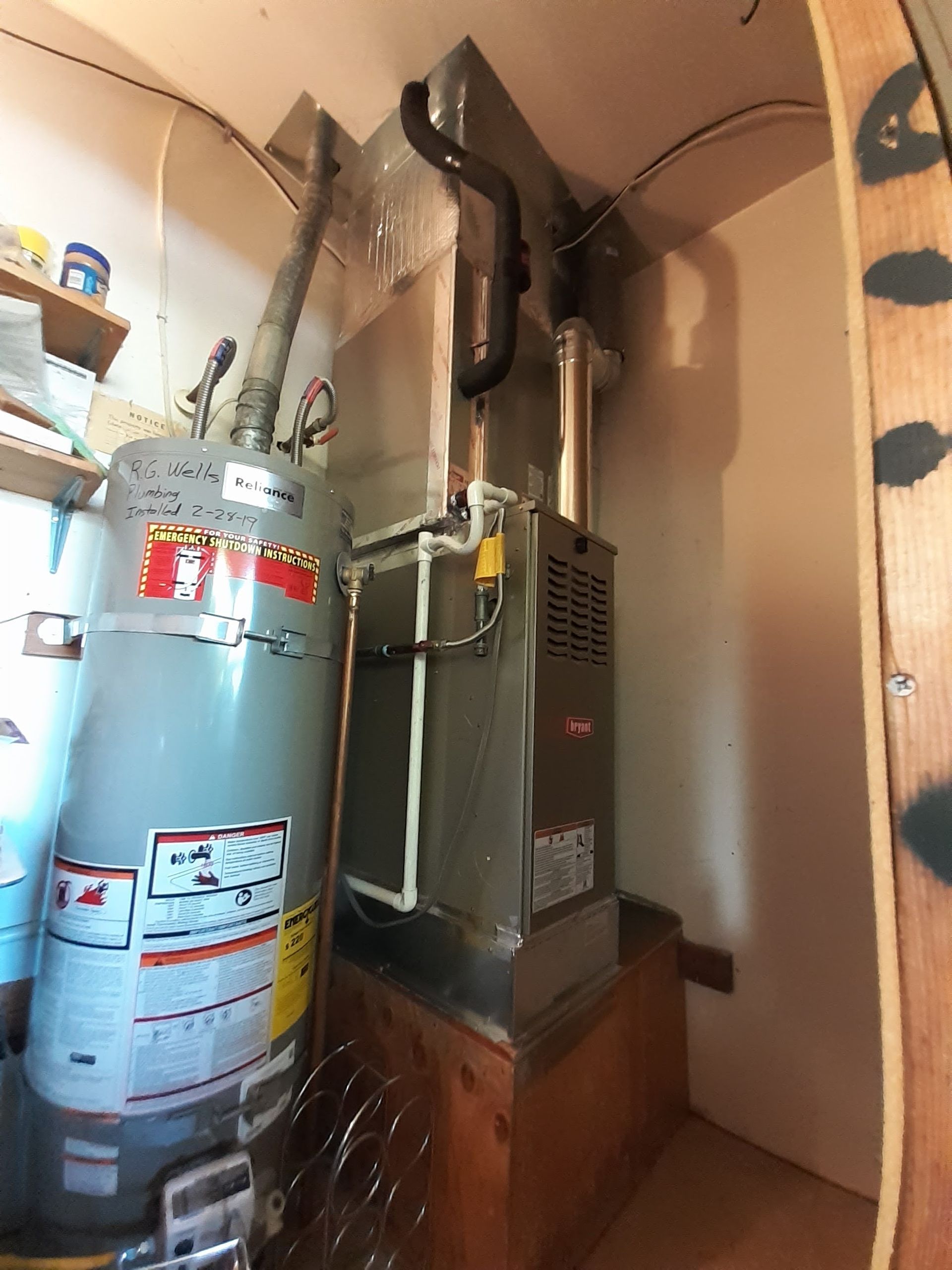 Utility closet with a water heater, furnace, and exposed ducts in a narrow alcove