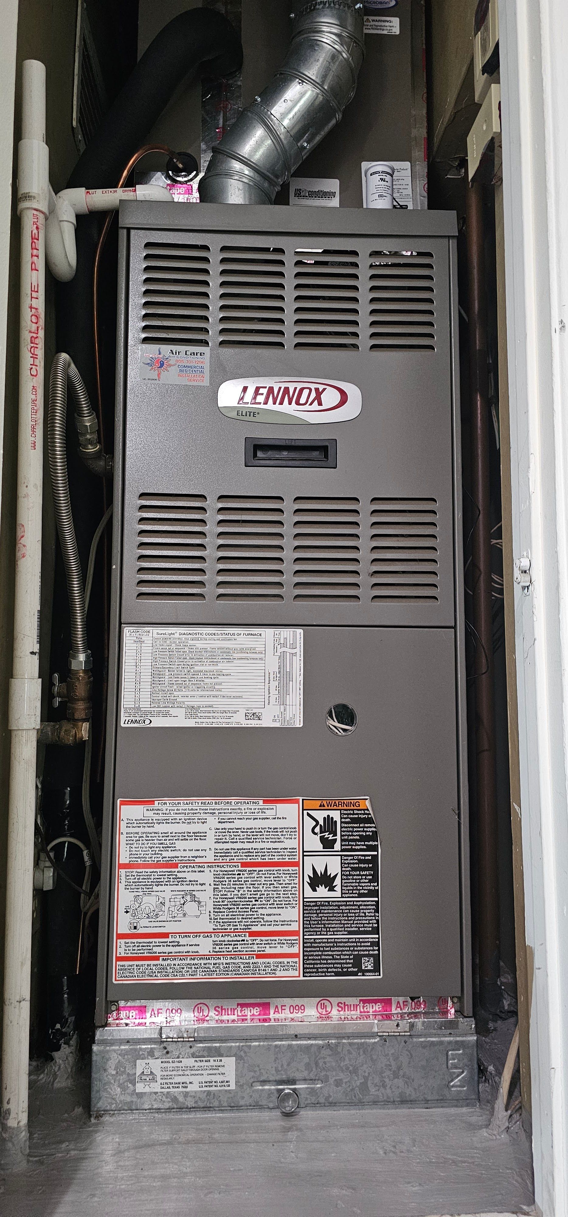 Gray Lennox furnace in a narrow utility closet with ductwork above and warning labels on the front.
