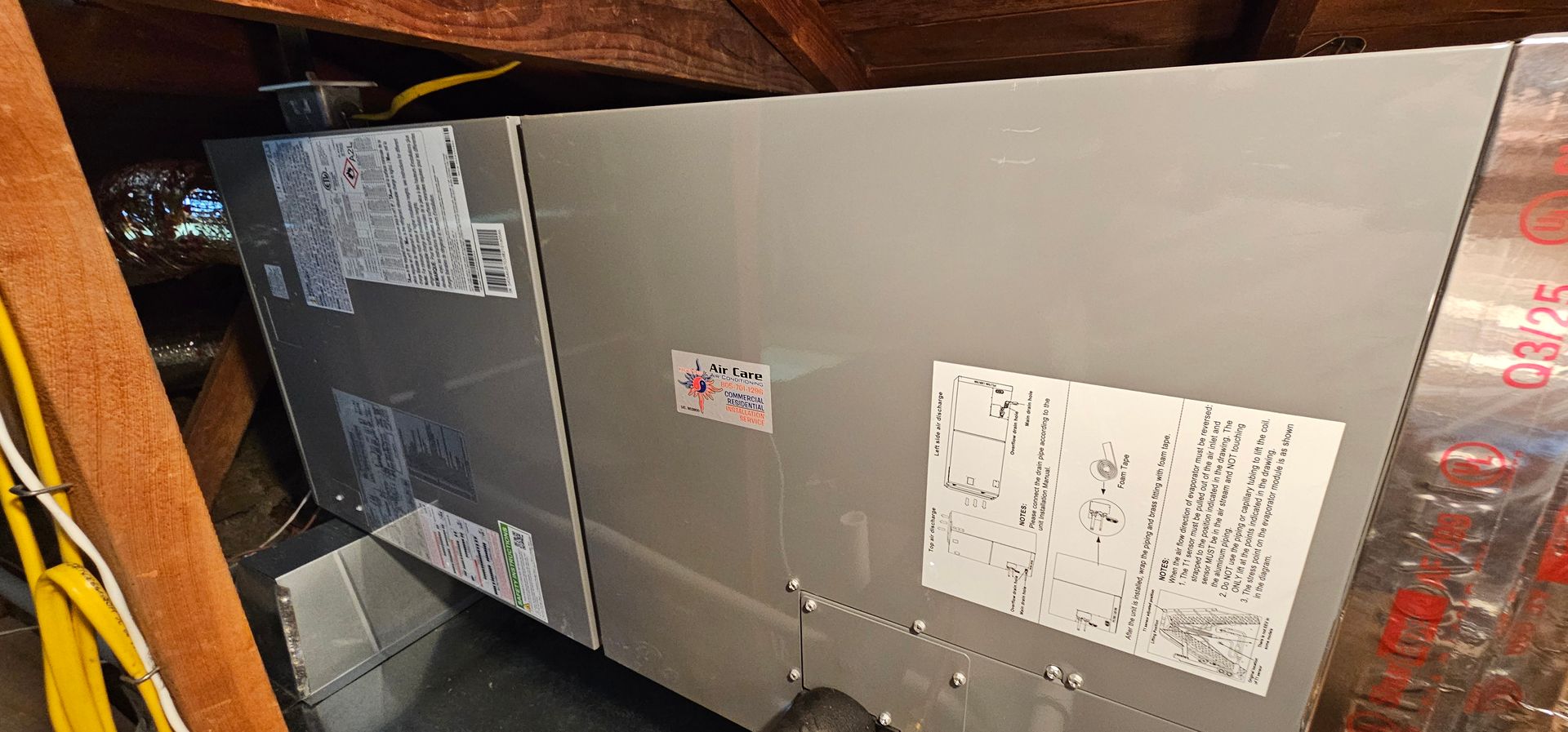 Two HVAC units in a cramped attic, one gray and one black with labels and ductwork.