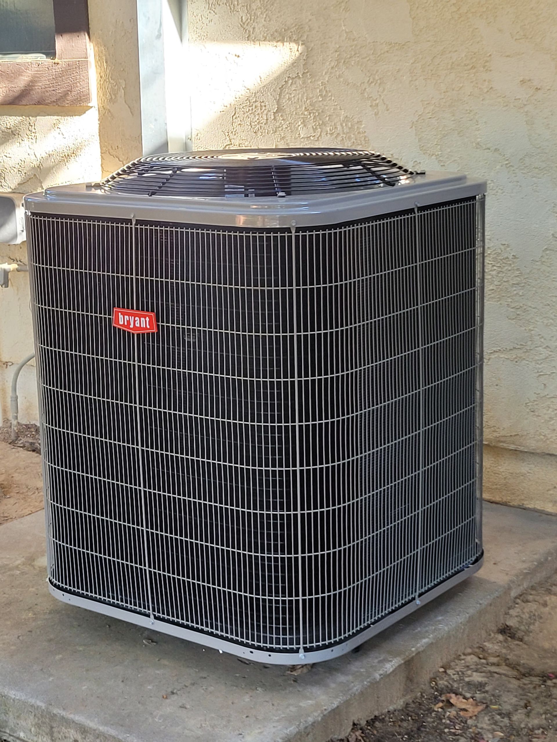 Outdoor air conditioner condenser unit on a concrete pad beside a stucco wall.