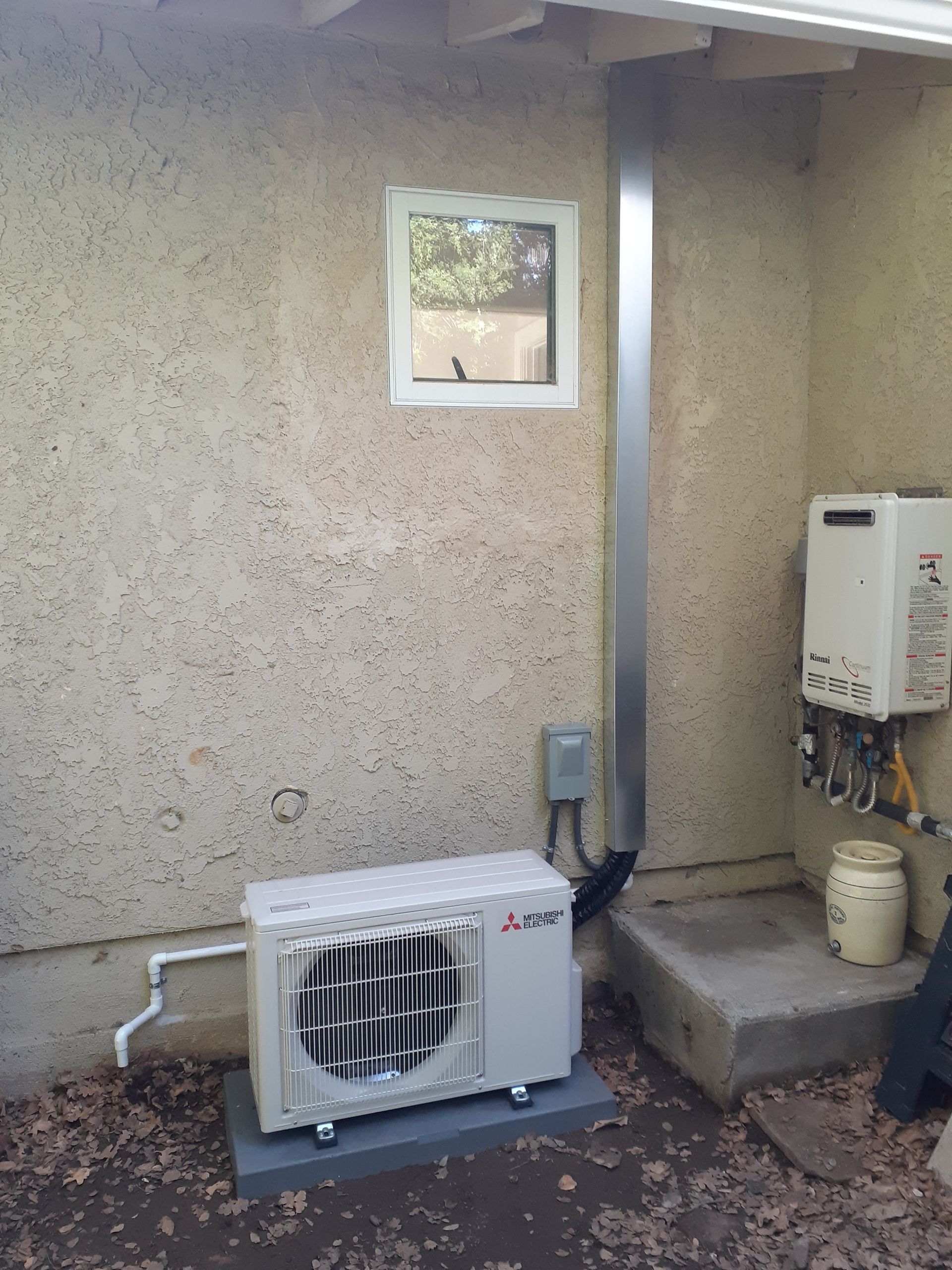Outdoor wall with a small window, HVAC units, and utility equipment beside a concrete step.