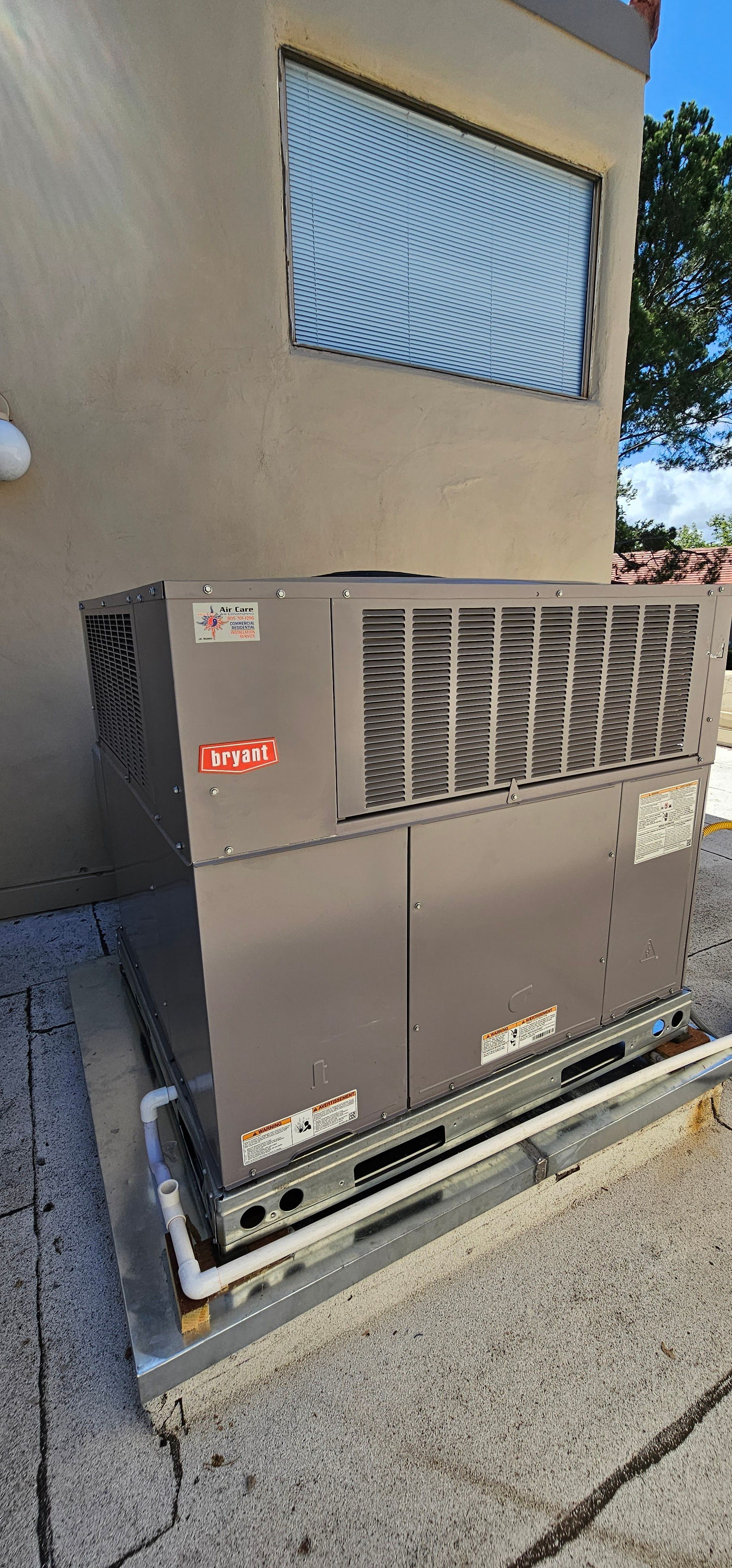 Two HVAC units beside a beige building wall under a window, on a concrete pad.