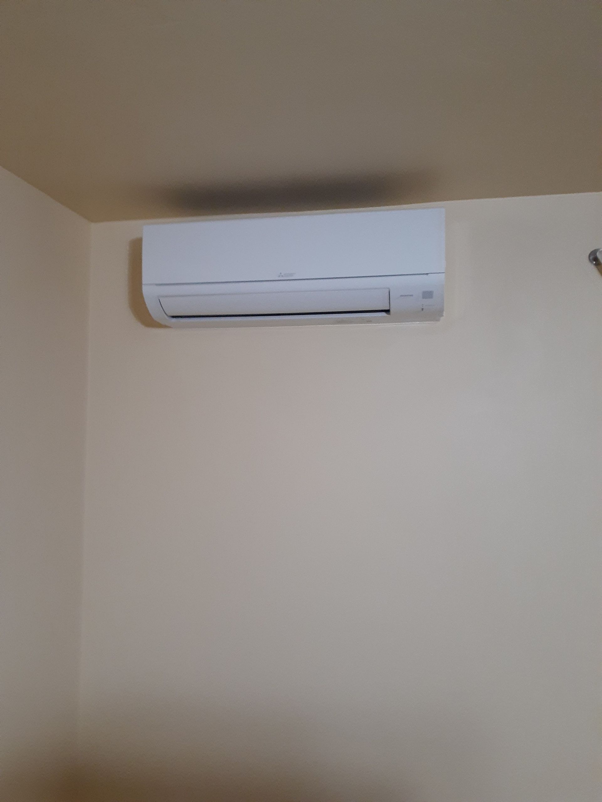 Wall-mounted white air conditioner near the ceiling on a beige wall.