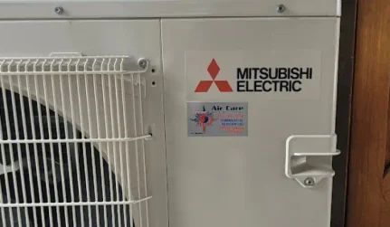 Mitsubishi Electric outdoor air conditioner unit with white grille and beige panel.