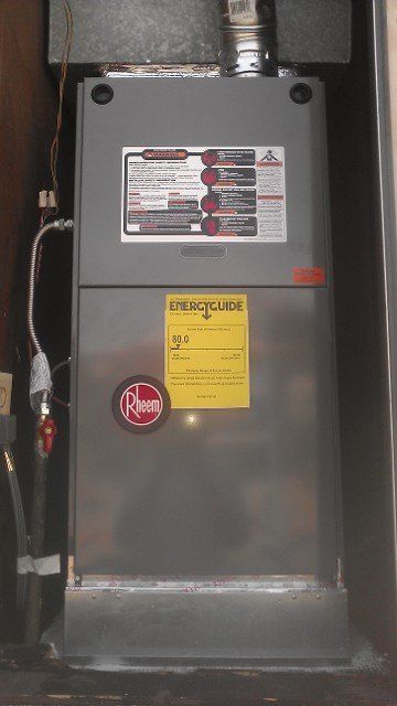 Gray Rheem furnace with labels and vent pipe in a utility closet.