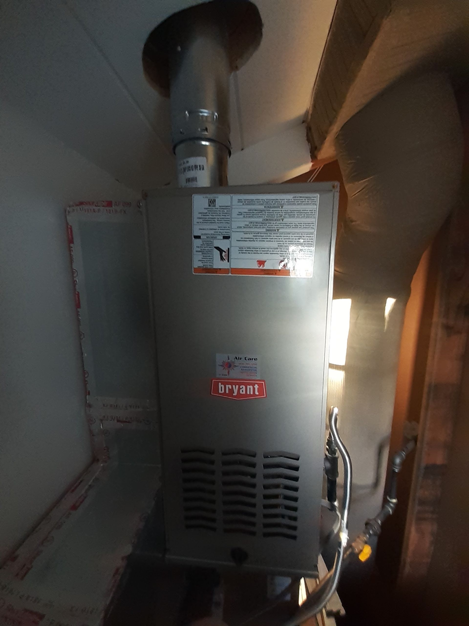 Wall-mounted gas furnace with vent pipe and labels in a narrow utility closet.