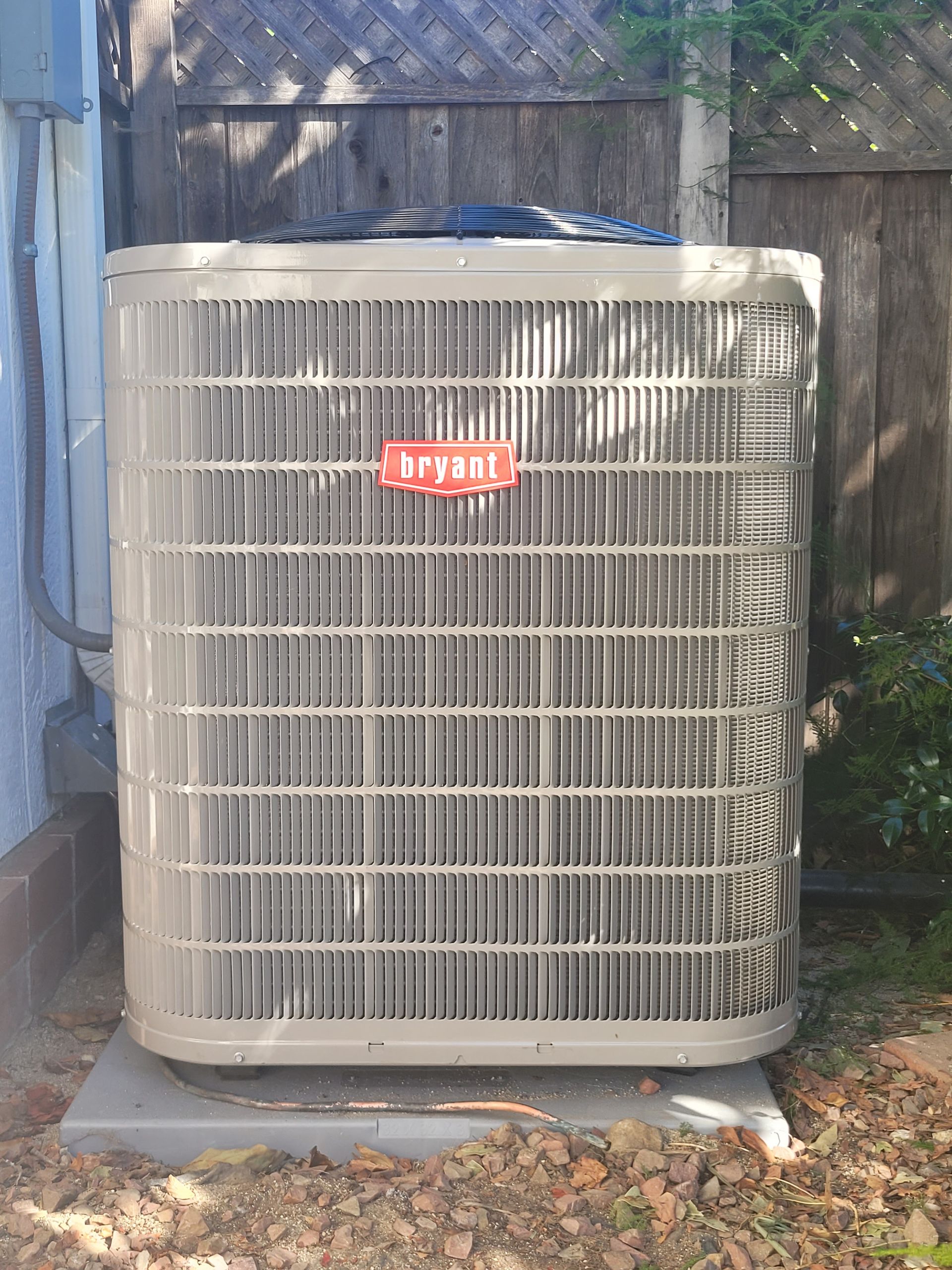 Large beige outdoor air conditioner unit beside a blue wall and fence.