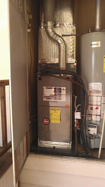 Residential utility closet with furnace, water heater, and exposed ductwork in a tight space