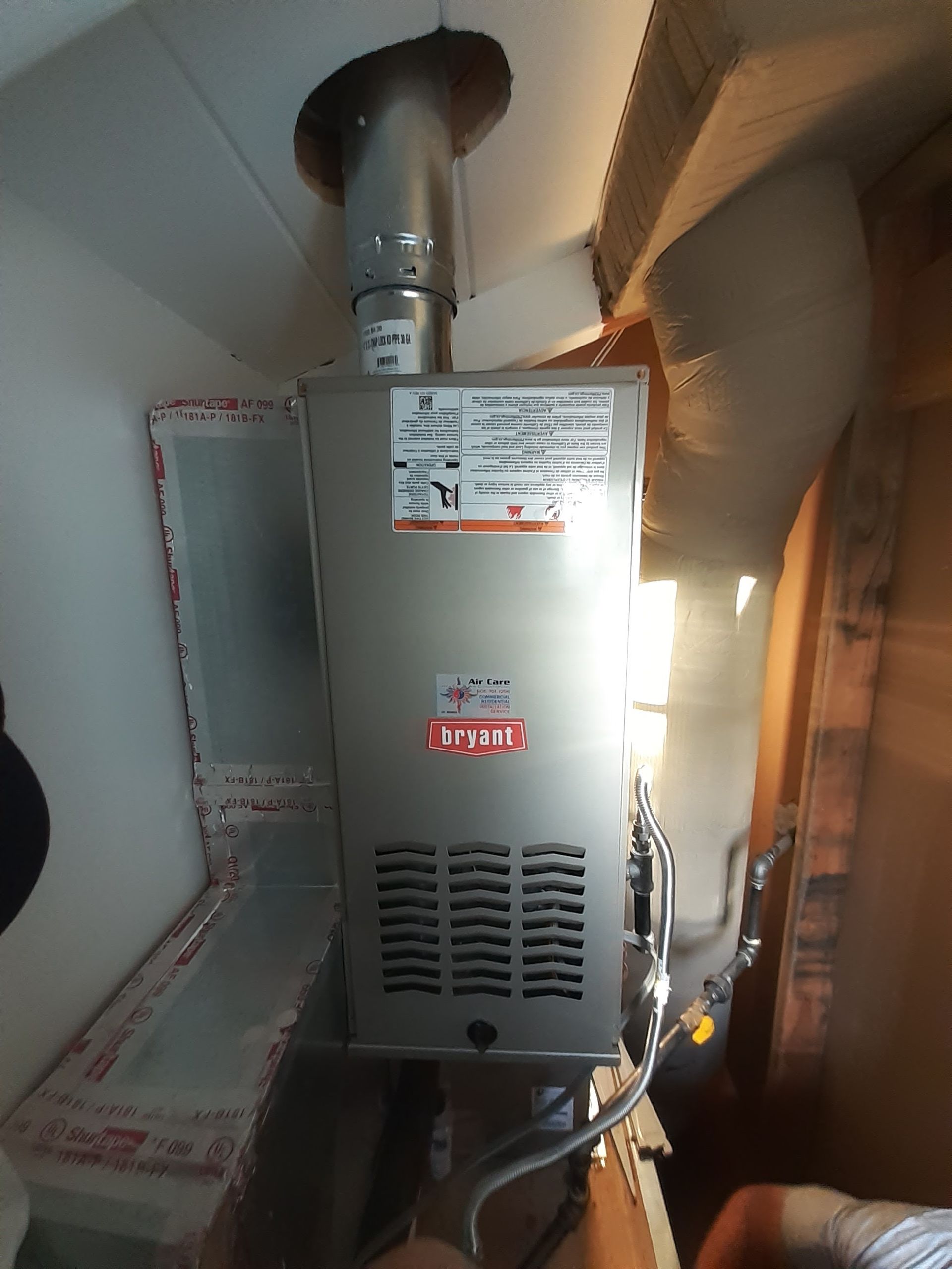 Gray wall-mounted furnace with vent pipes in a utility closet, lit from the right side