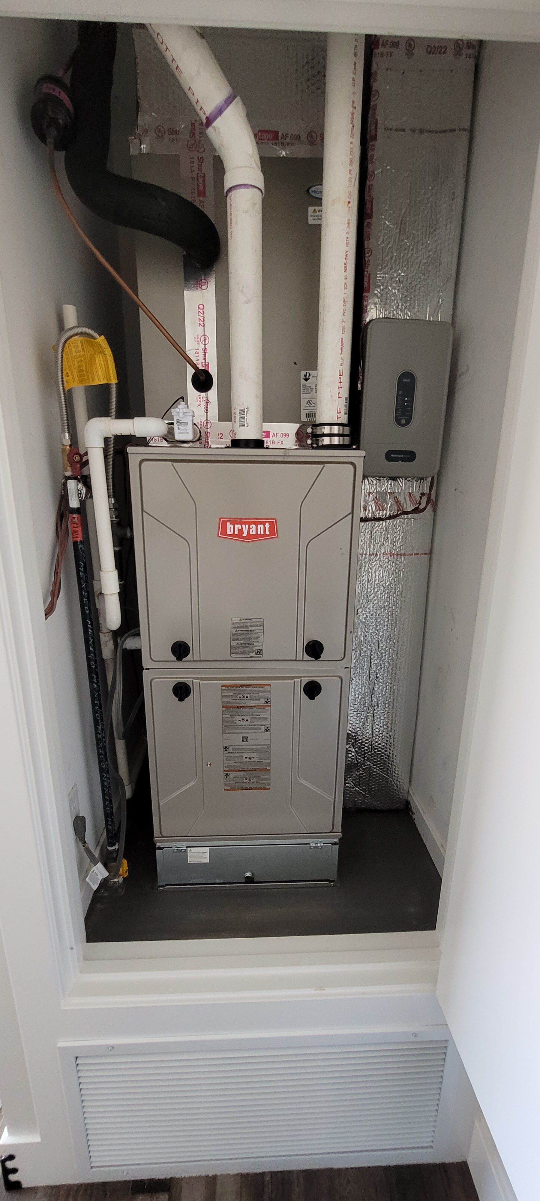 Furnace unit in a narrow utility closet with exposed white and black pipes above.